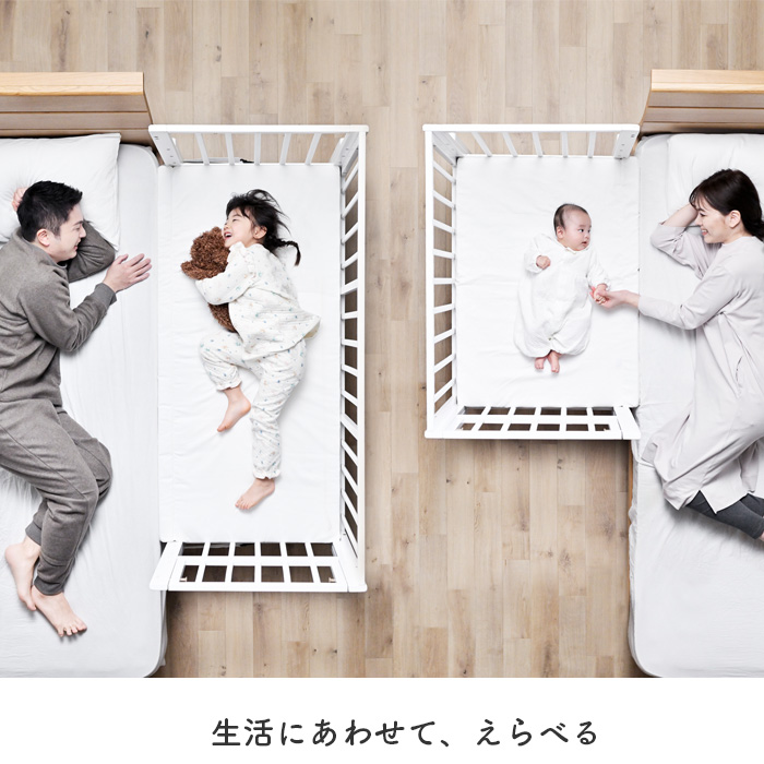 ベビーベッドに寝る子どもと添い寝するパパとママ